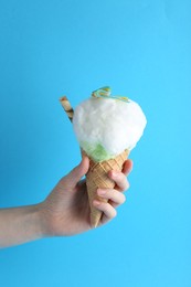 Woman holding waffle cone with cotton candy on light blue background, closeup