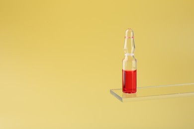 Photo of Glass ampoule with liquid on yellow background. Space for text