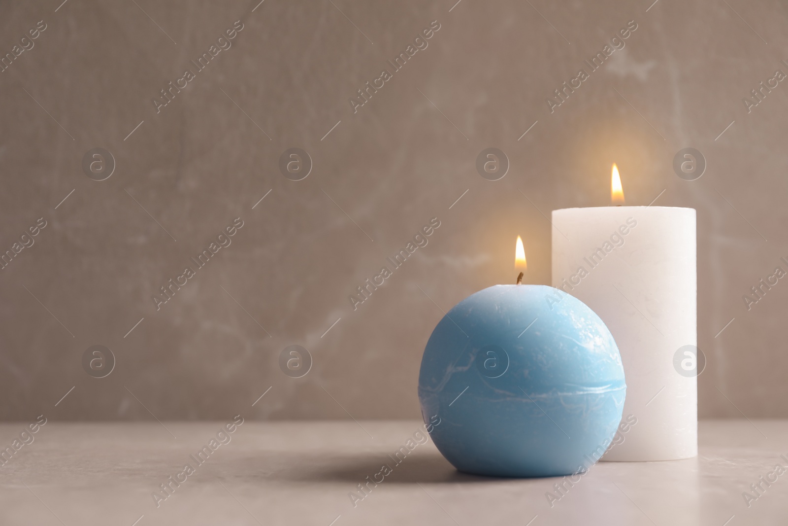 Photo of Beautiful burning wax candles on table against grey background