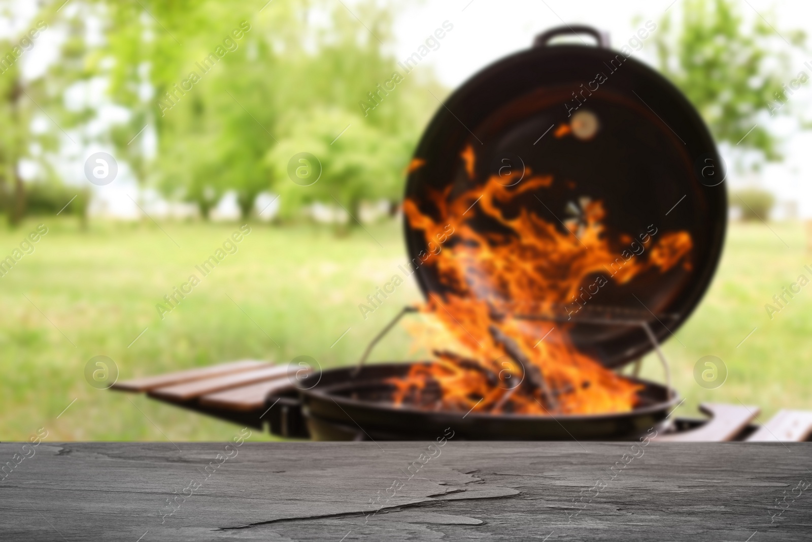 Image of Empty wooden table and blurred view of modern barbecue grill with fire flames outdoors