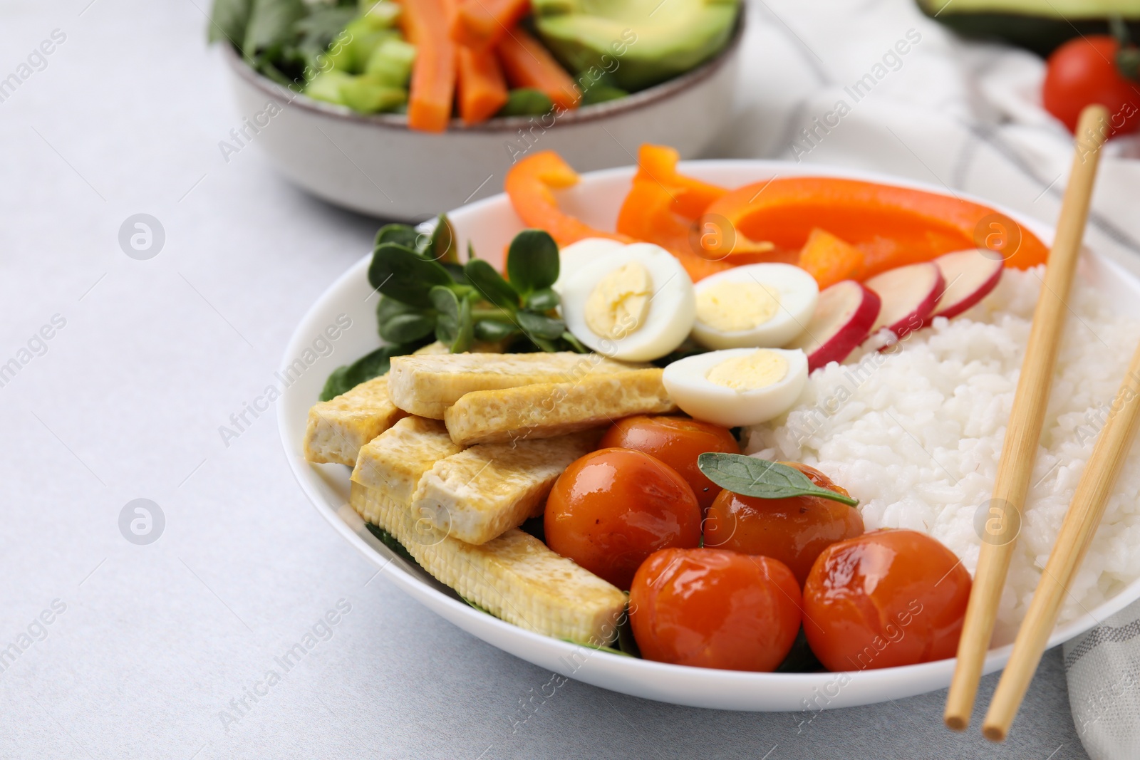 Photo of Delicious poke bowl with basil, vegetables, eggs and tofu on light grey table, closeup