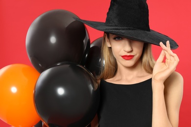 Photo of Beautiful woman wearing witch costume with balloons for Halloween party on red background