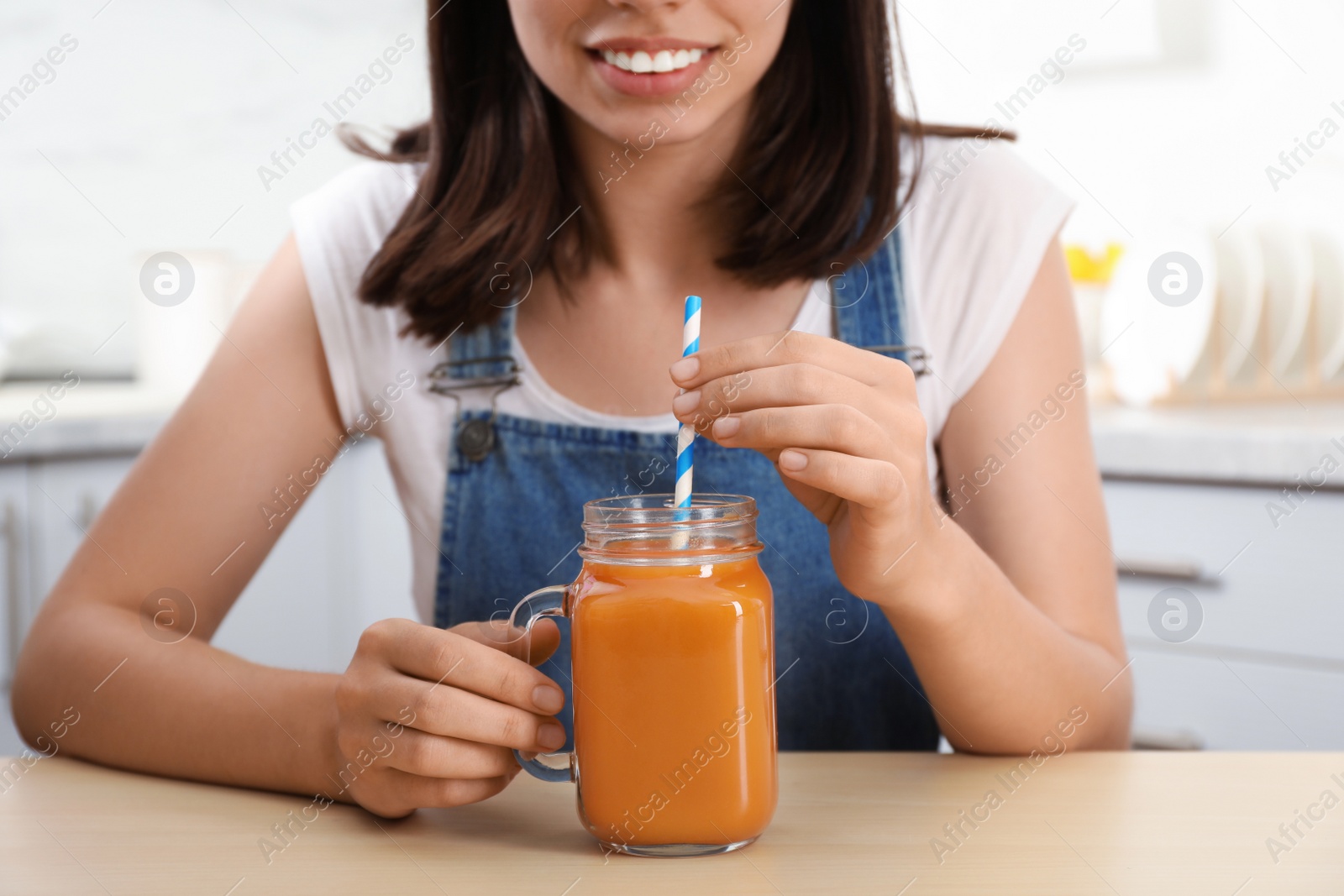 Photo of Woman with mason jar of tasty carrot juice at table indoors, closeup