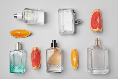 Flat lay composition with bottles of perfume and citrus fruits on light background