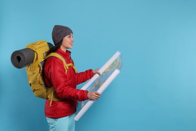 Photo of Smiling young woman with backpack and map on light blue background, space for text. Active tourism