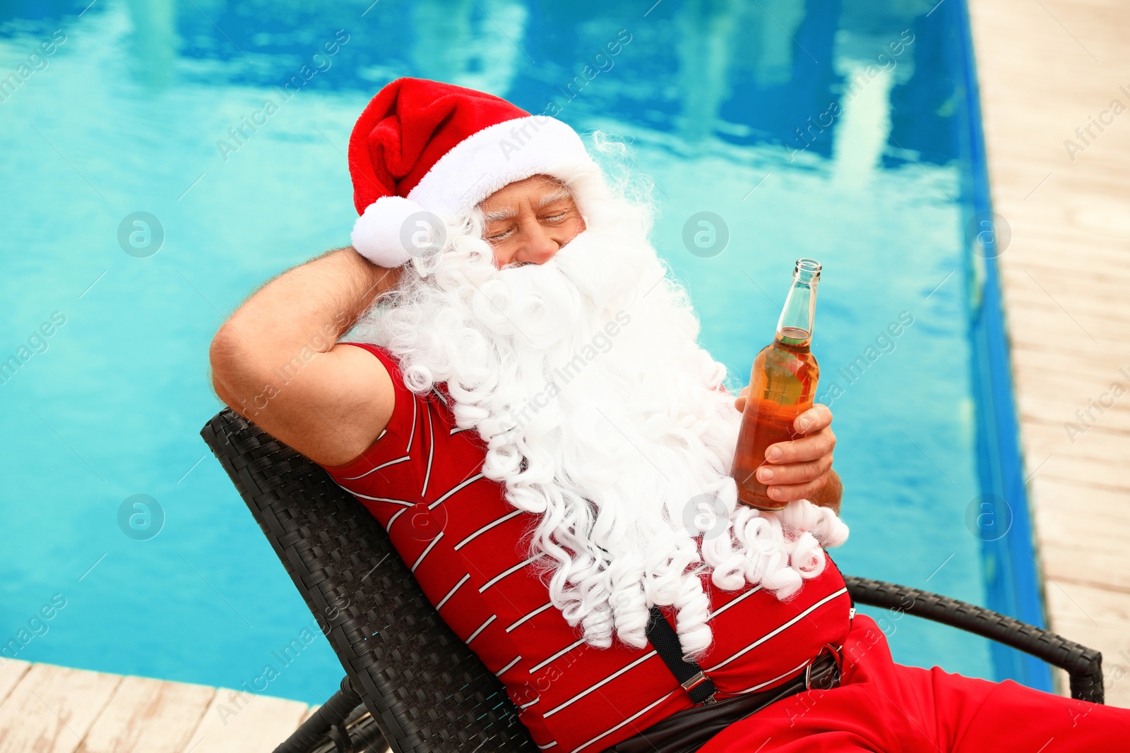 Photo of Authentic Santa Claus with bottle of beer near pool at resort