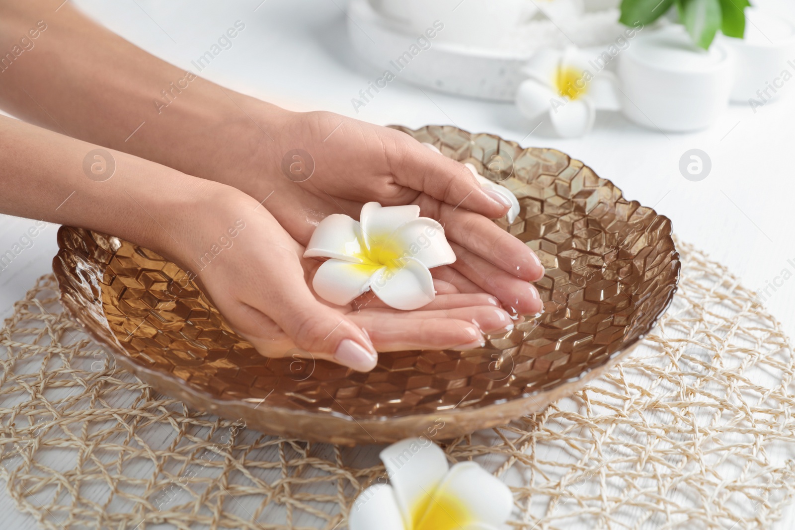 Photo of Woman soaking her hands in bowl with water and flowers on table, closeup. Spa treatment