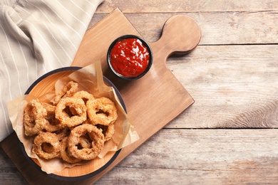 Homemade crunchy fried onion rings in plate and sauce on wooden background, top view. Space for text