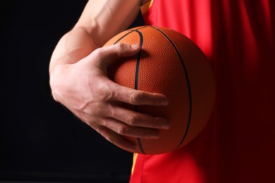 Photo of Athletic man with basketball ball on black background, closeup