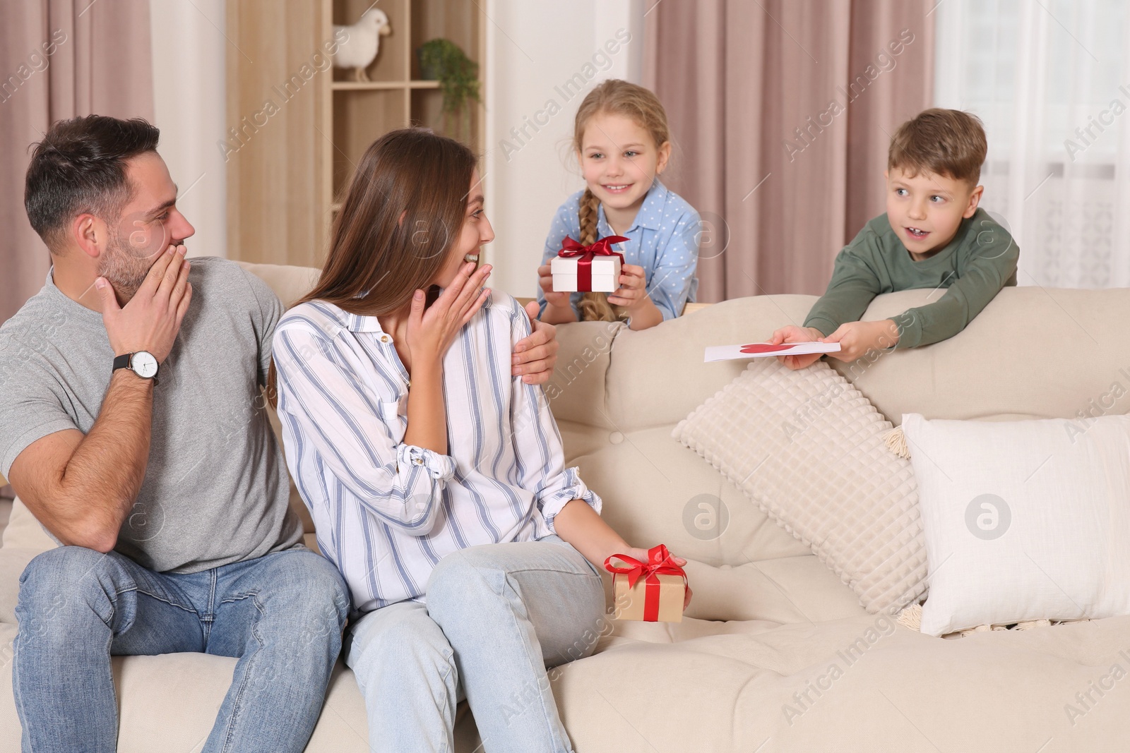 Photo of Cute little children presenting their parents with gifts on sofa at home