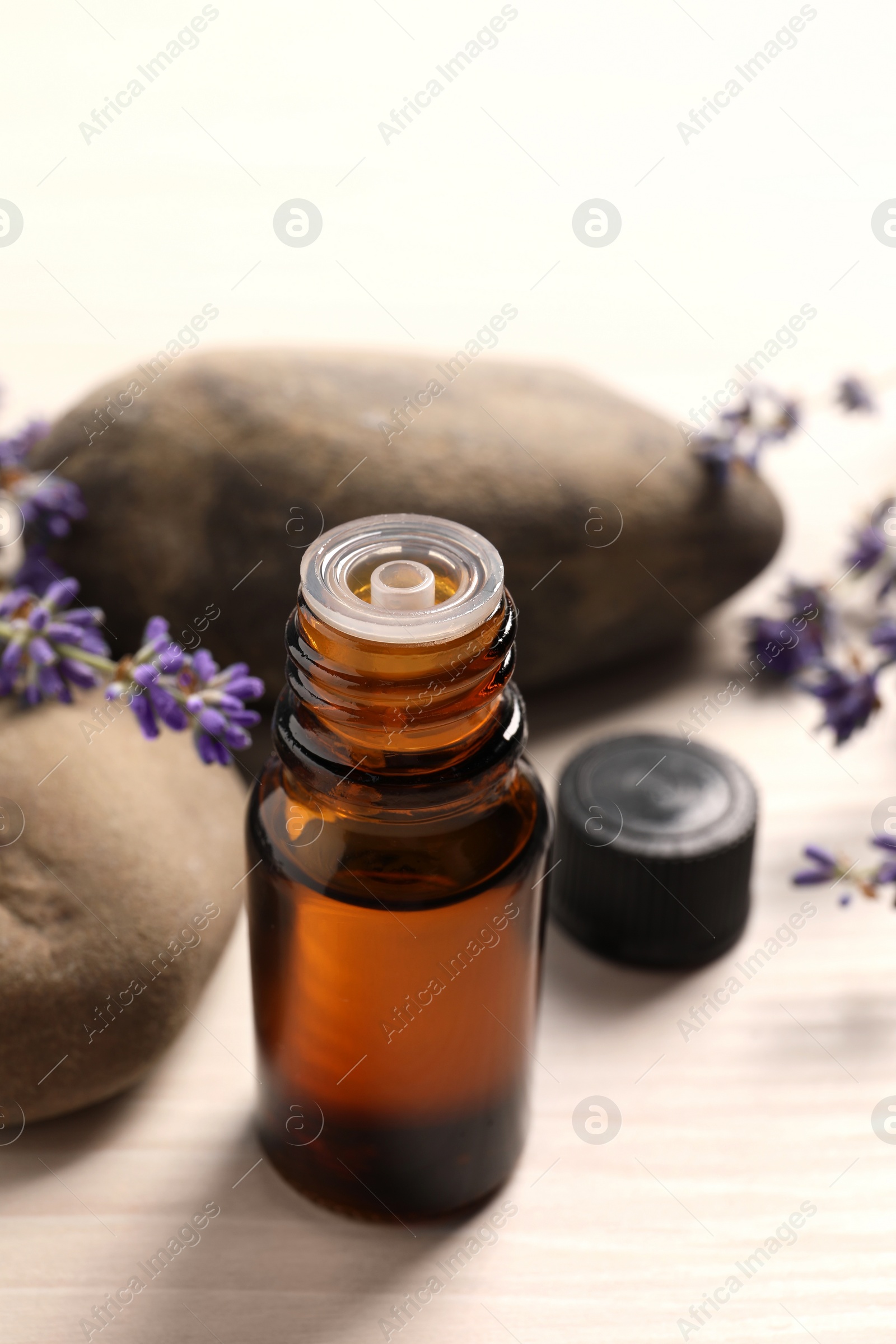 Photo of Bottle of essential oil and lavender flowers on white wooden table, closeup. Space for text