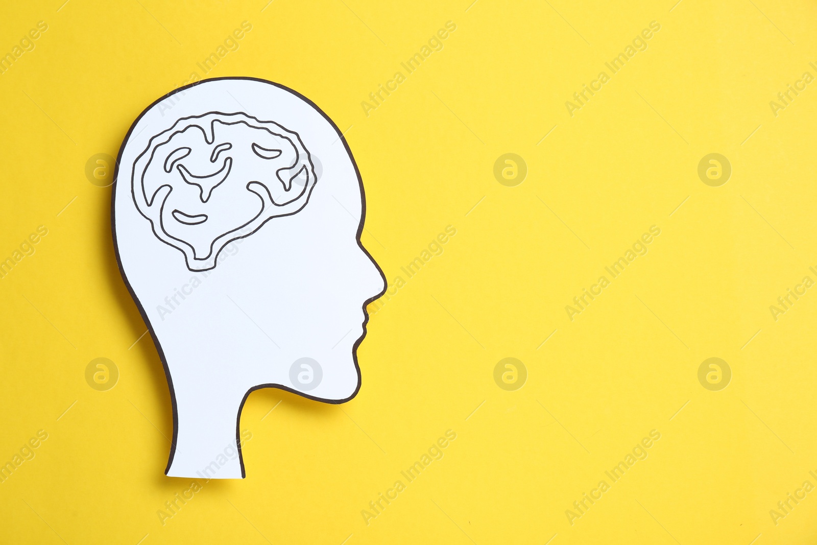 Photo of Paper human head cutout with drawing of brain on yellow background, top view. Space for text