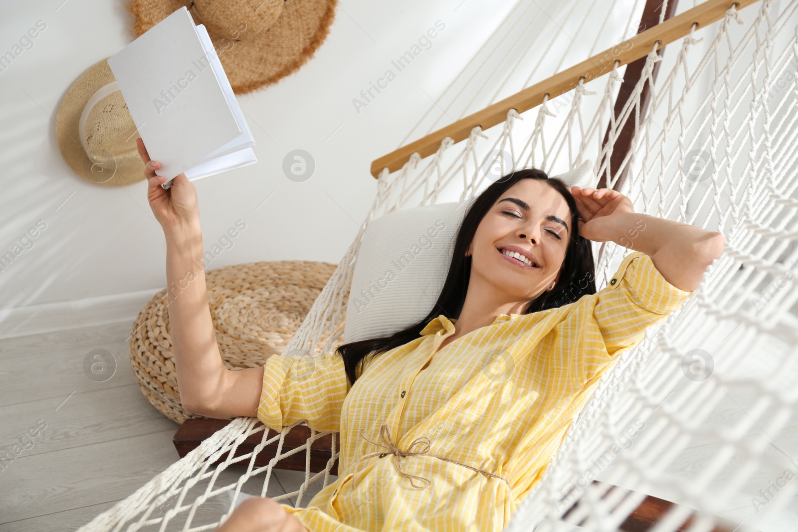 Photo of Young woman reading book in hammock at home