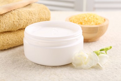 Photo of Body care. Moisturizing cream in open jar and flower on light textured table, closeup