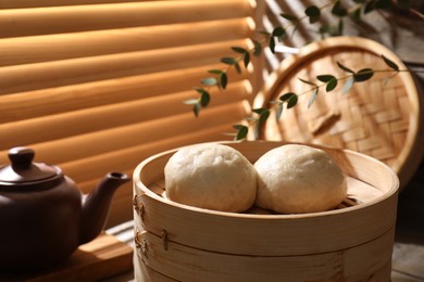 Delicious Chinese steamed buns and kettle on table, closeup
