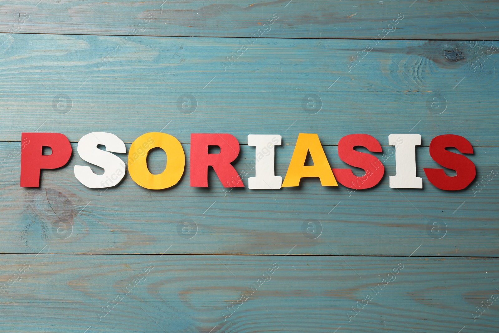 Photo of Word Psoriasis made of paper letters on light blue wooden table, top view