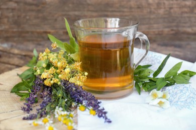 Photo of Cup of hot aromatic tea and different fresh herbs on wooden background