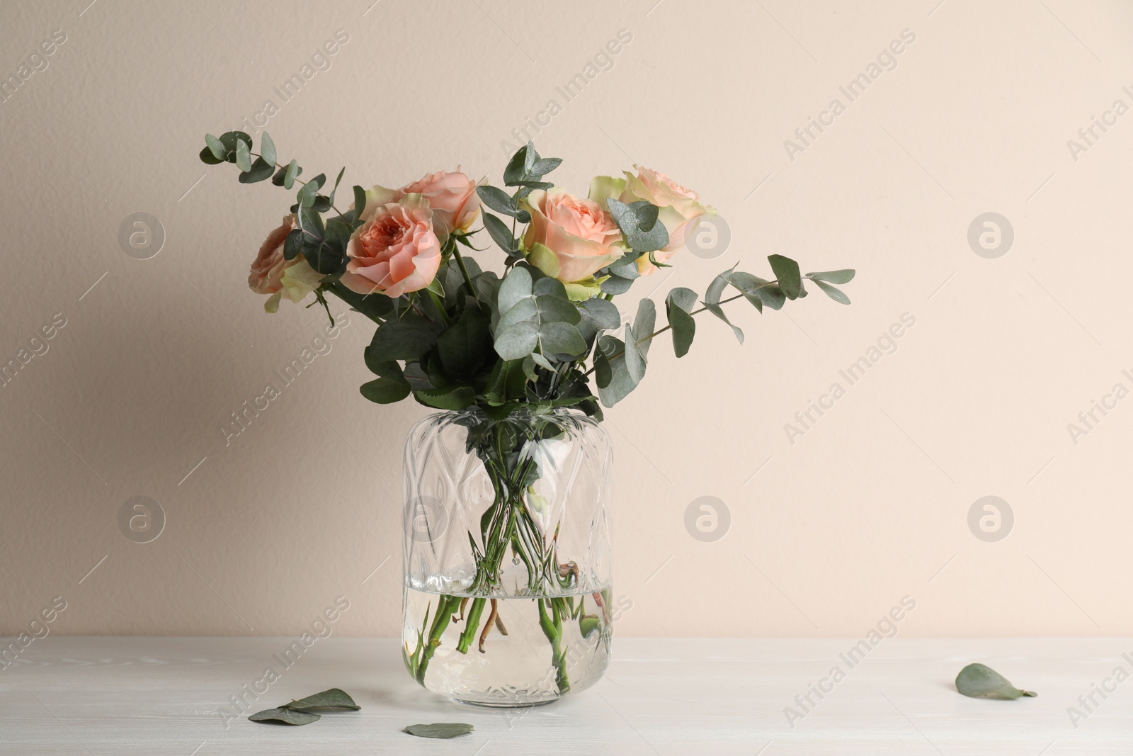 Photo of Vase with bouquet of beautiful roses on white wooden table near beige wall