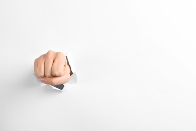 Woman showing clenched fist through hole in torn white paper, space for text. Victory concept