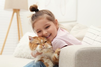 Happy little girl hugging cute cat on sofa at home