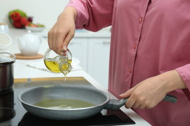 Photo of Woman pouring oil from jug into frying pan in kitchen, closeup