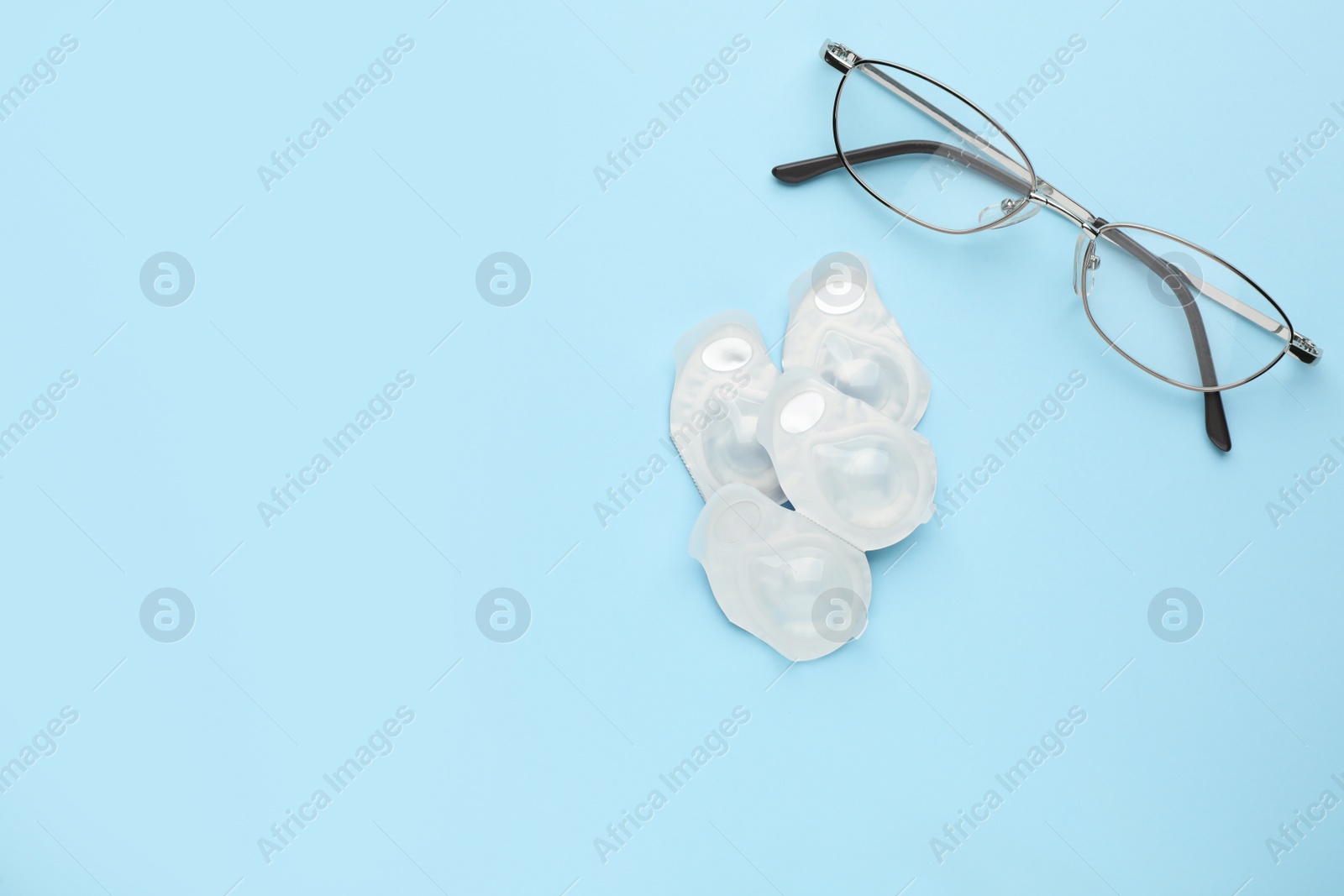 Photo of Packages with contact lenses and glasses on light blue background, flat lay. Space for text