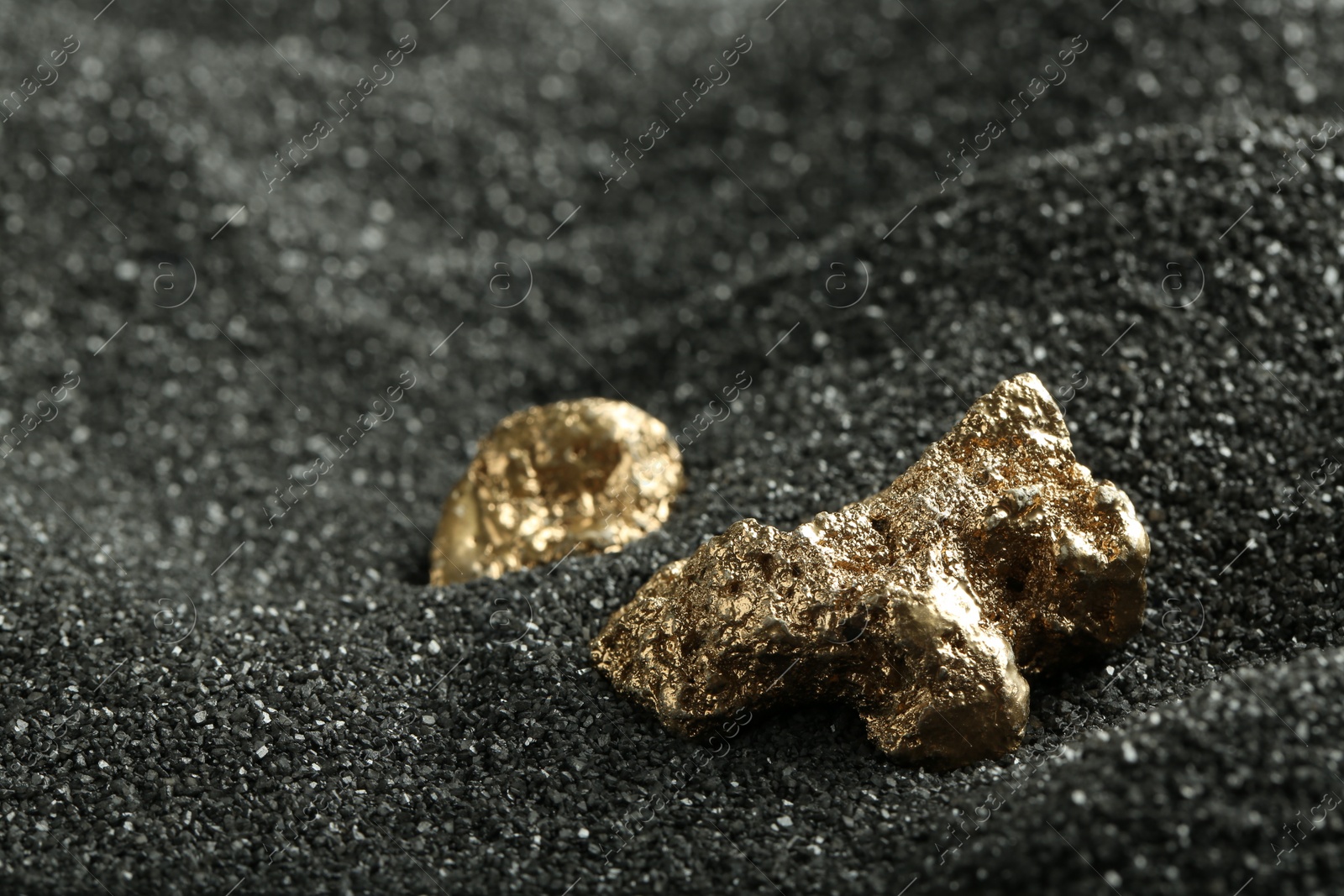 Photo of Shiny gold nuggets on black sand, closeup. Space for text