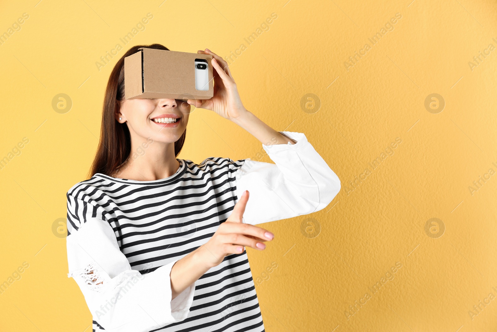 Photo of Young woman using cardboard virtual reality headset on color background. Space for text