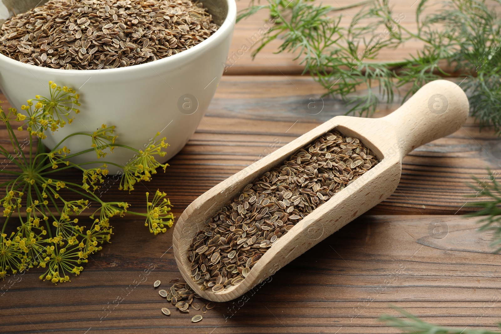 Photo of Scoop of dry seeds, bowl and fresh dill on wooden table