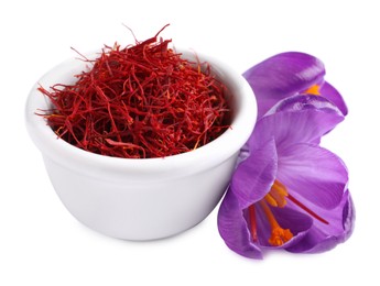 Dried saffron in bowl and crocus flowers on white background