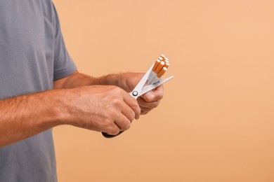 Photo of Stop smoking concept. Man cutting cigarettes on light brown background, closeup. Space for text