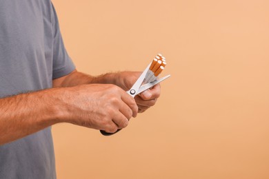 Stop smoking concept. Man cutting cigarettes on light brown background, closeup. Space for text