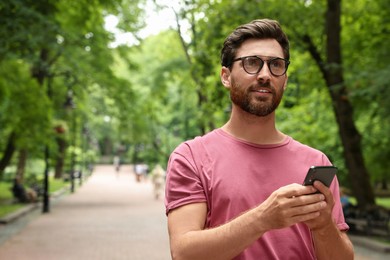 Photo of Handsome man using smartphone in park, space for text
