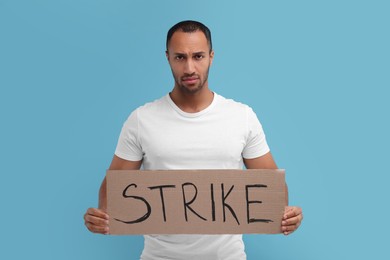 Photo of Upset man holding cardboard banner with word Strike on light blue background