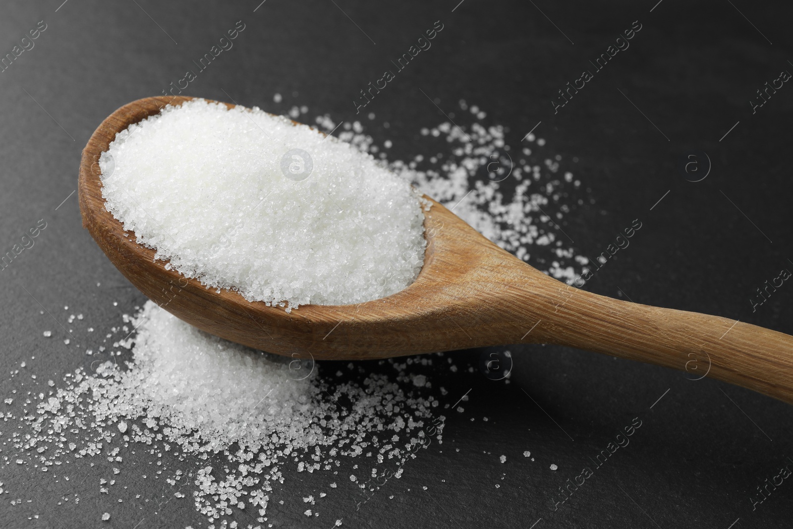 Photo of Spoon with granulated sugar on black table, closeup