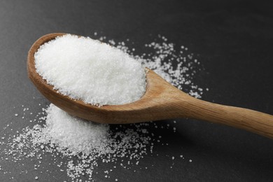 Spoon with granulated sugar on black table, closeup