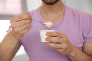 Photo of Young man with tasty yogurt on blurred background, closeup