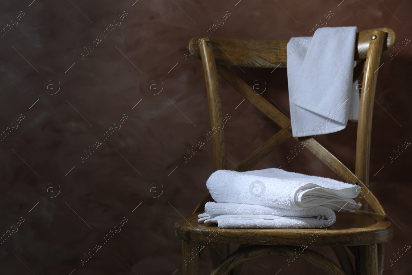 Photo of White terry towels on wooden chair against brown background. Space for text