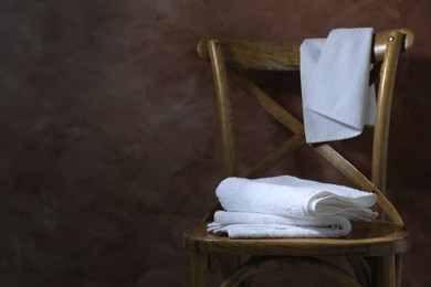 Photo of White terry towels on wooden chair against brown background. Space for text