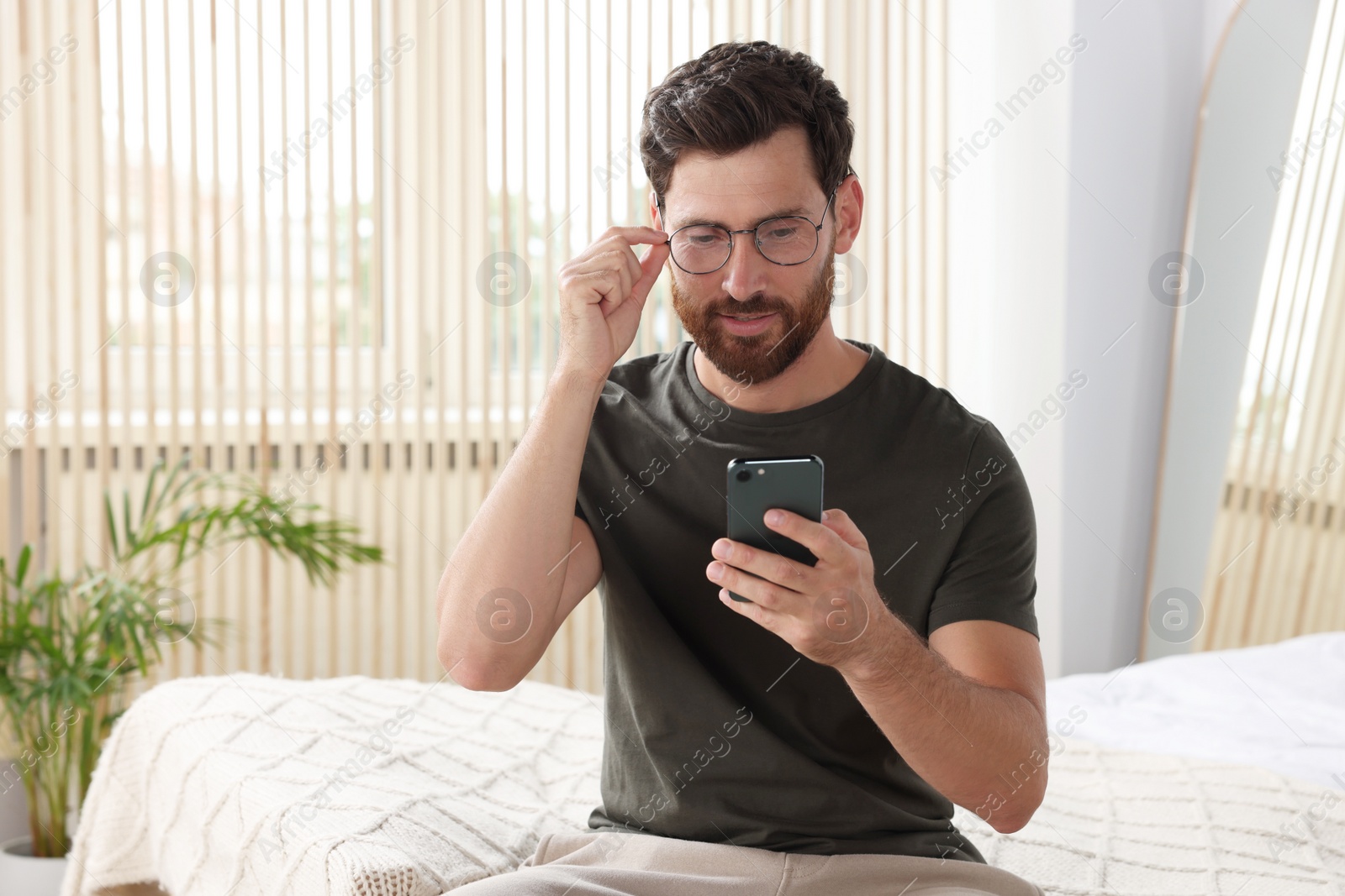 Photo of Handsome man using smartphone at home, space for text