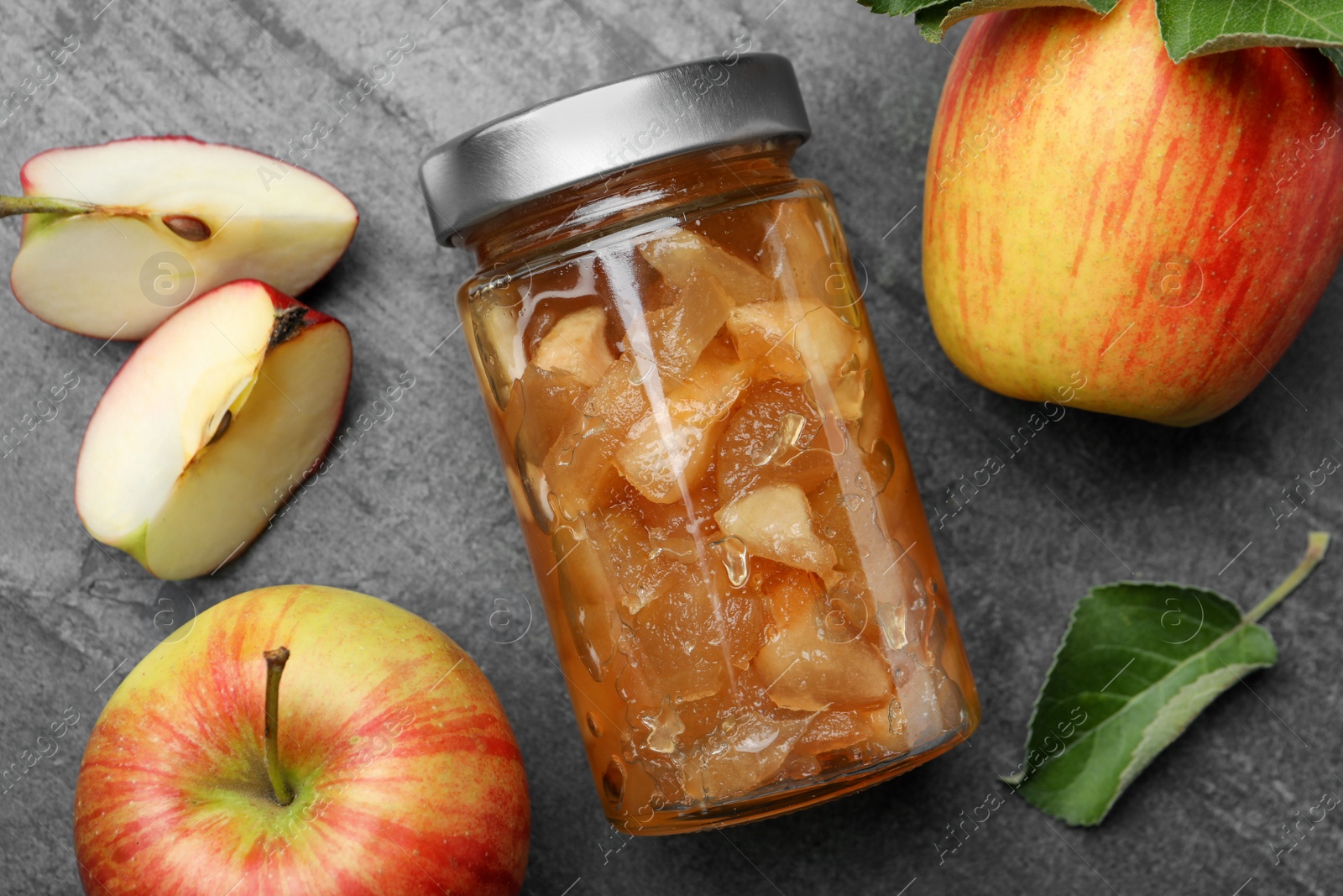 Photo of Tasty apple jam in glass jar and fresh fruits on grey table, flat lay