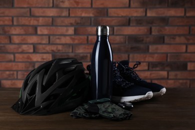 Photo of Different cycling accessories on wooden table against brick wall