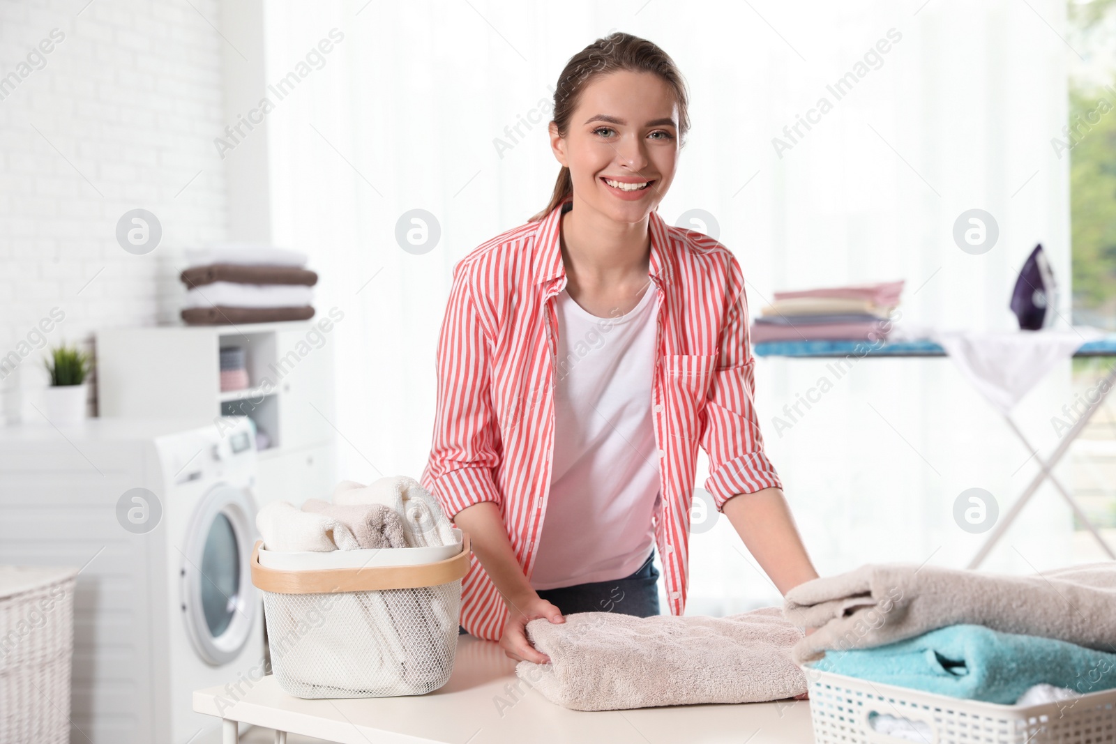 Photo of Happy woman folding clean towel at table indoors. Laundry day