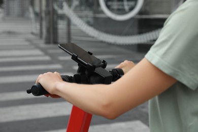 Woman riding modern electric kick scooter with smartphone outdoors