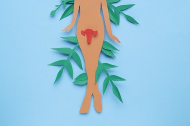 Photo of Woman's health. Female paper figure with uterus and leaves on light blue background, flat lay