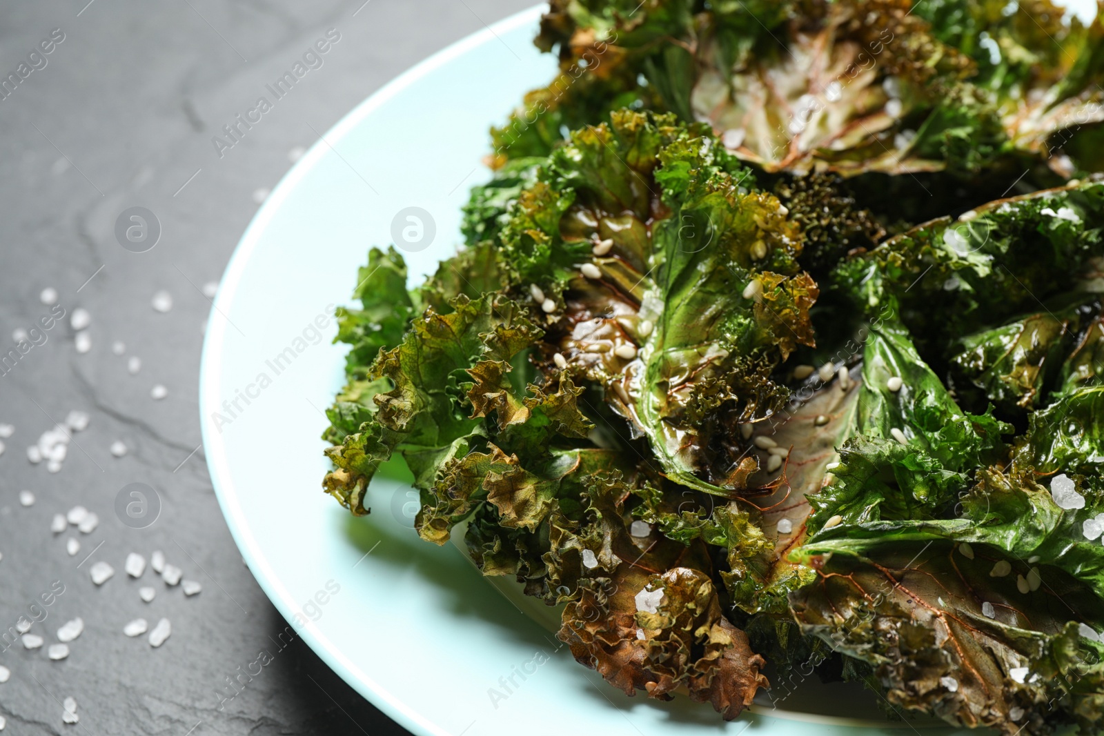 Photo of Tasty baked kale chips on dark grey table, closeup