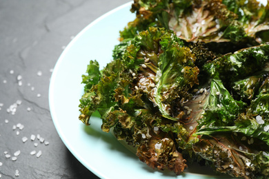 Photo of Tasty baked kale chips on dark grey table, closeup