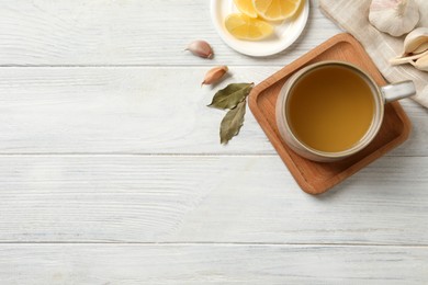 Photo of Hot delicious bouillon in cup on white wooden table, flat lay. Space for text