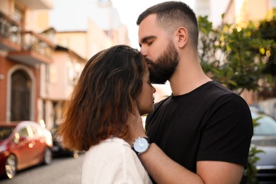 Photo of Handsome young man kissing his beautiful girlfriend on city street