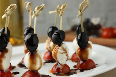 Tasty canapes with black olives, mozzarella and cherry tomatoes on table, closeup